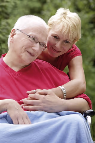Pflegerin umarmt in Rollstuhl sitzenden Klienten